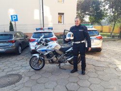 Na zdjęciu widać policjanta ruchu drogowego stojącego w kombinezonie motocyklowym przy motocyklu służbowym.