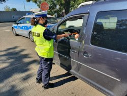Zdjęcie przedstawia policjantkę ruchu drogowego wręczającą ulotki prewencyjne i odblaski kierowcy.